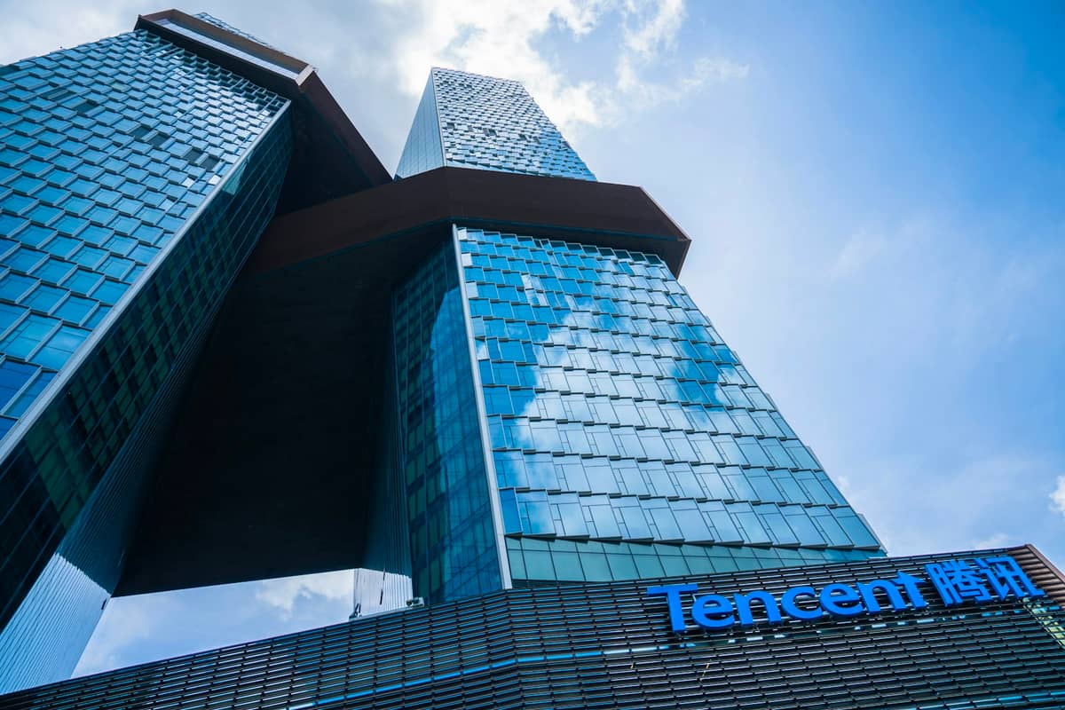 Vista em ângulo baixo das duas torres de vidro interligadas das Tencent Seafront Towers em Shenzhen, com o logotipo da Tencent visível, contra um céu azul.