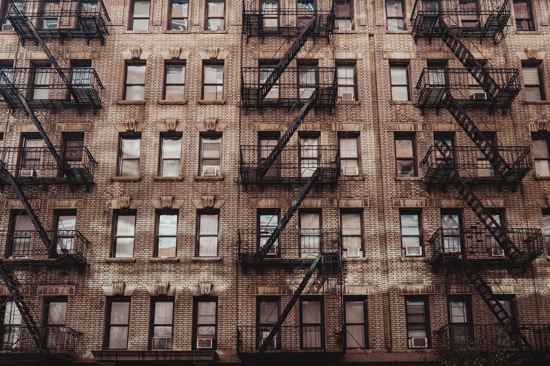 Classico edificio tenement di New York con più file di finestre e scale antincendio in metallo nero, che mostrano l'architettura storica in una luce uniforme.
