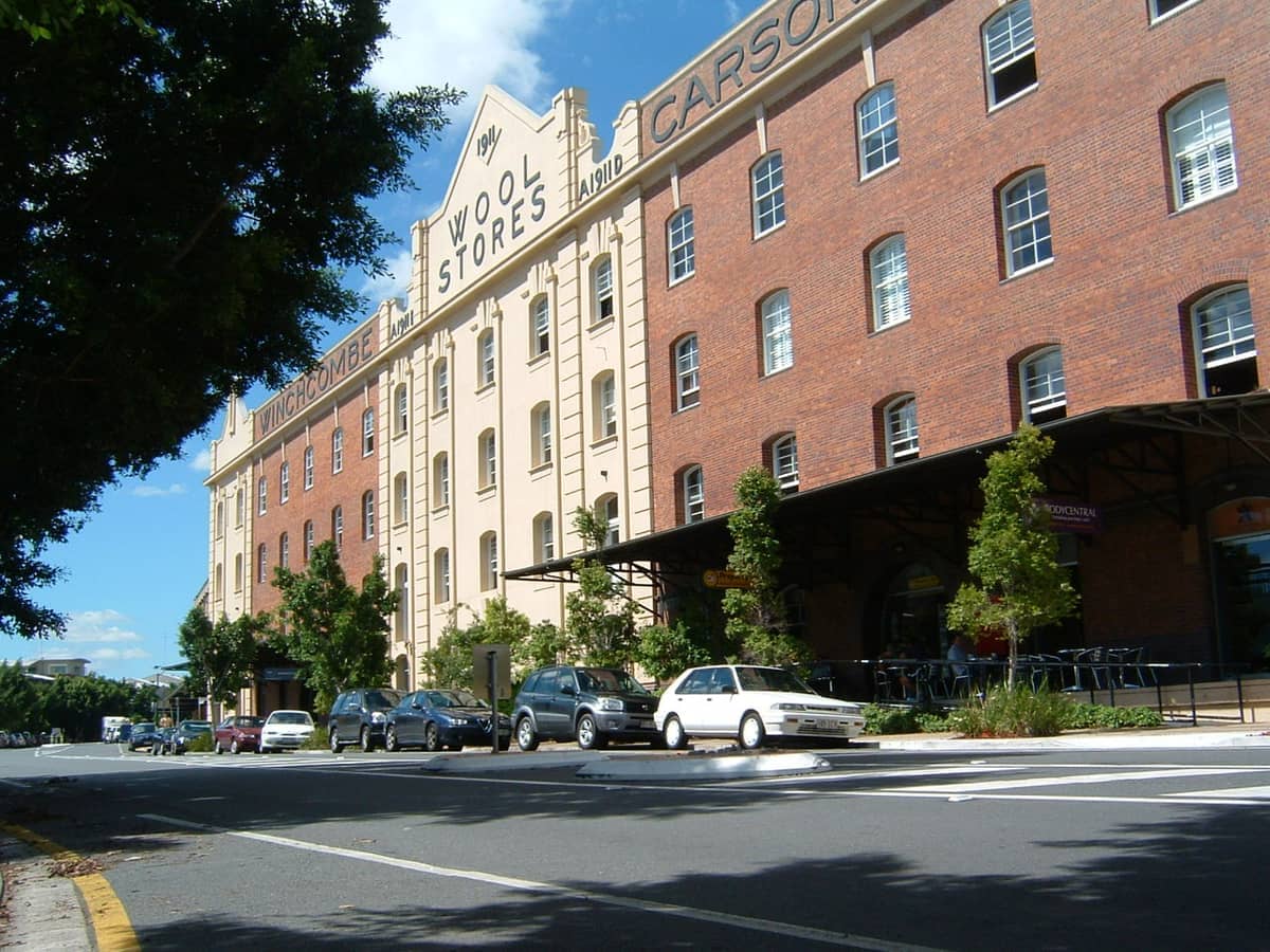 Die historischen Teneriffe Woolstores mit rot-cremefarbener Backsteinefassade, Straßenbäumen und geparkten Autos unter einem klaren blauen Himmel über Brisbane.
