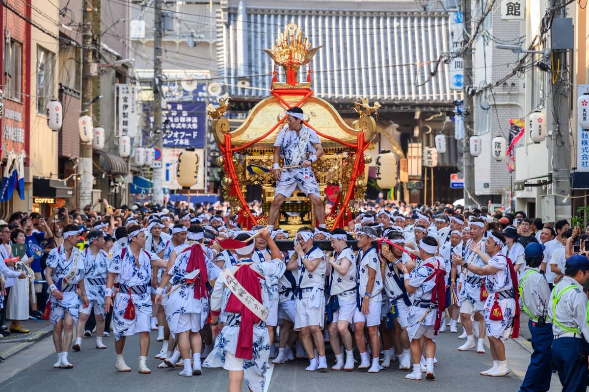 Crowds of participants in traditional clothing carry a large mikoshi portable shrine through Osaka streets during the Tenjin Matsuri festival procession.