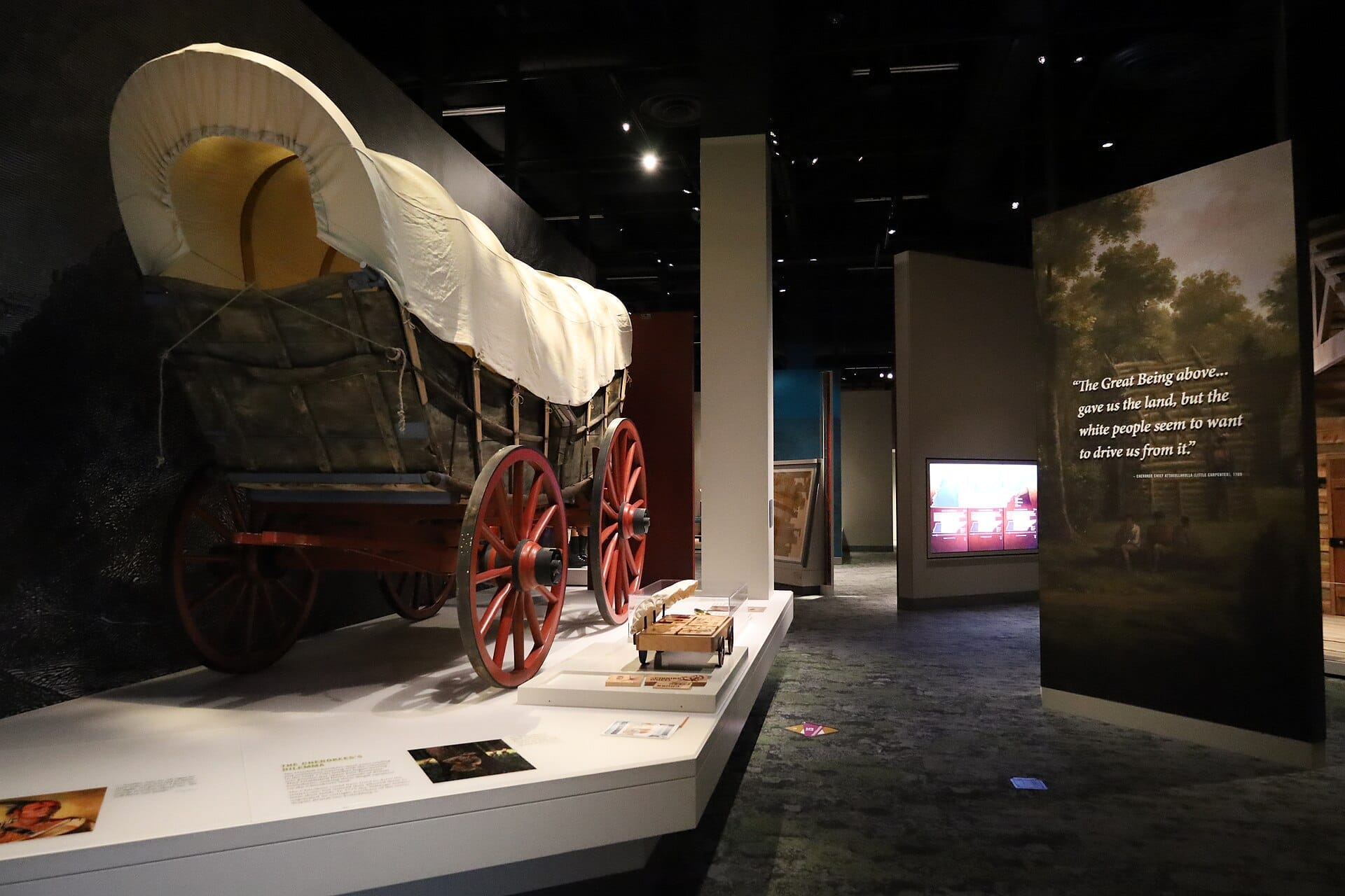 Exposición de carreta cubierta en el Tennessee State Museum, con ruedas de madera rojas y paneles educativos en un espacio de exposición tenuemente iluminado.