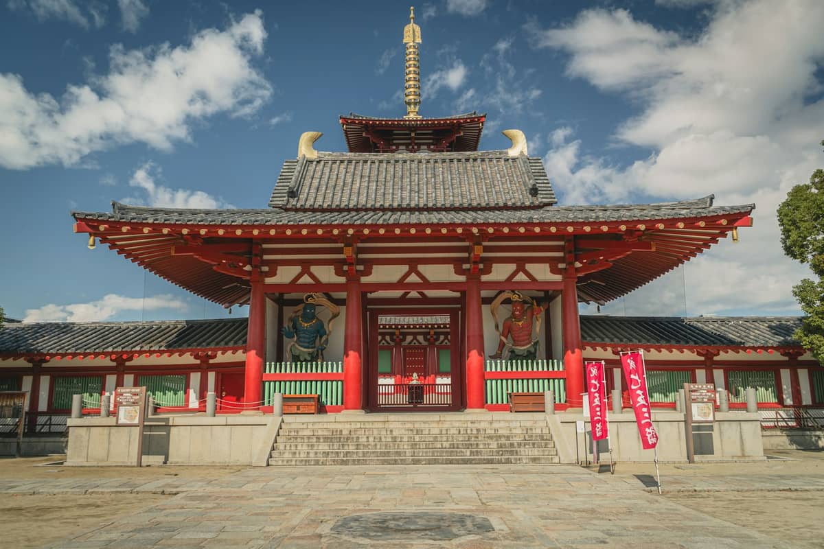 Front view of Shitennoji Temple’s main hall, showing traditional red-and-white architecture and guardian statues, under a blue sky in Tennoji, Osaka.