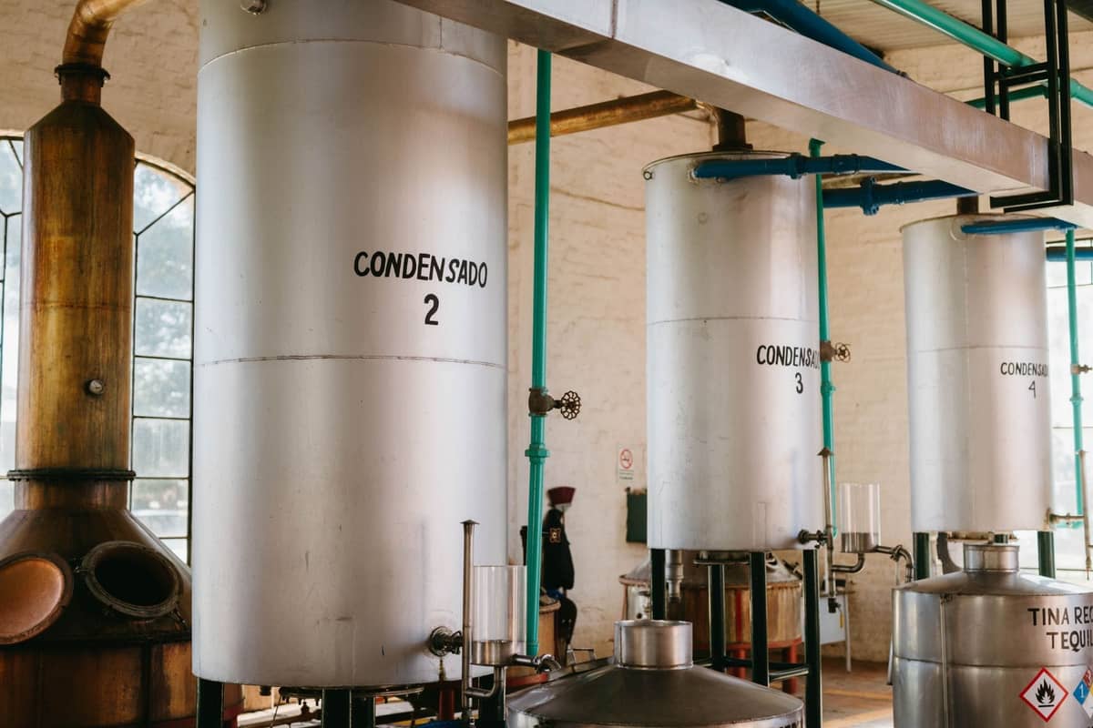 ภายในโรงกลั่นเตกีลาที่แสดงถังสแตนเลสขนาดใหญ่ที่มีป้ายว่า 'condensado' และท่อระบบอุตสาหกรรม