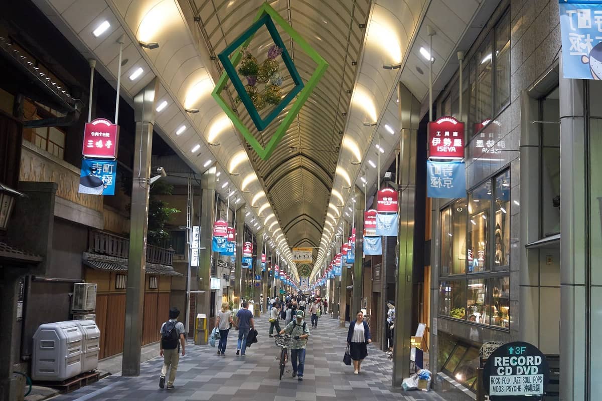 Covered walkway of Teramachi Shopping Arcade in Kyoto, lined with store signs, modern lighting, and people walking under the illuminated arched roof.