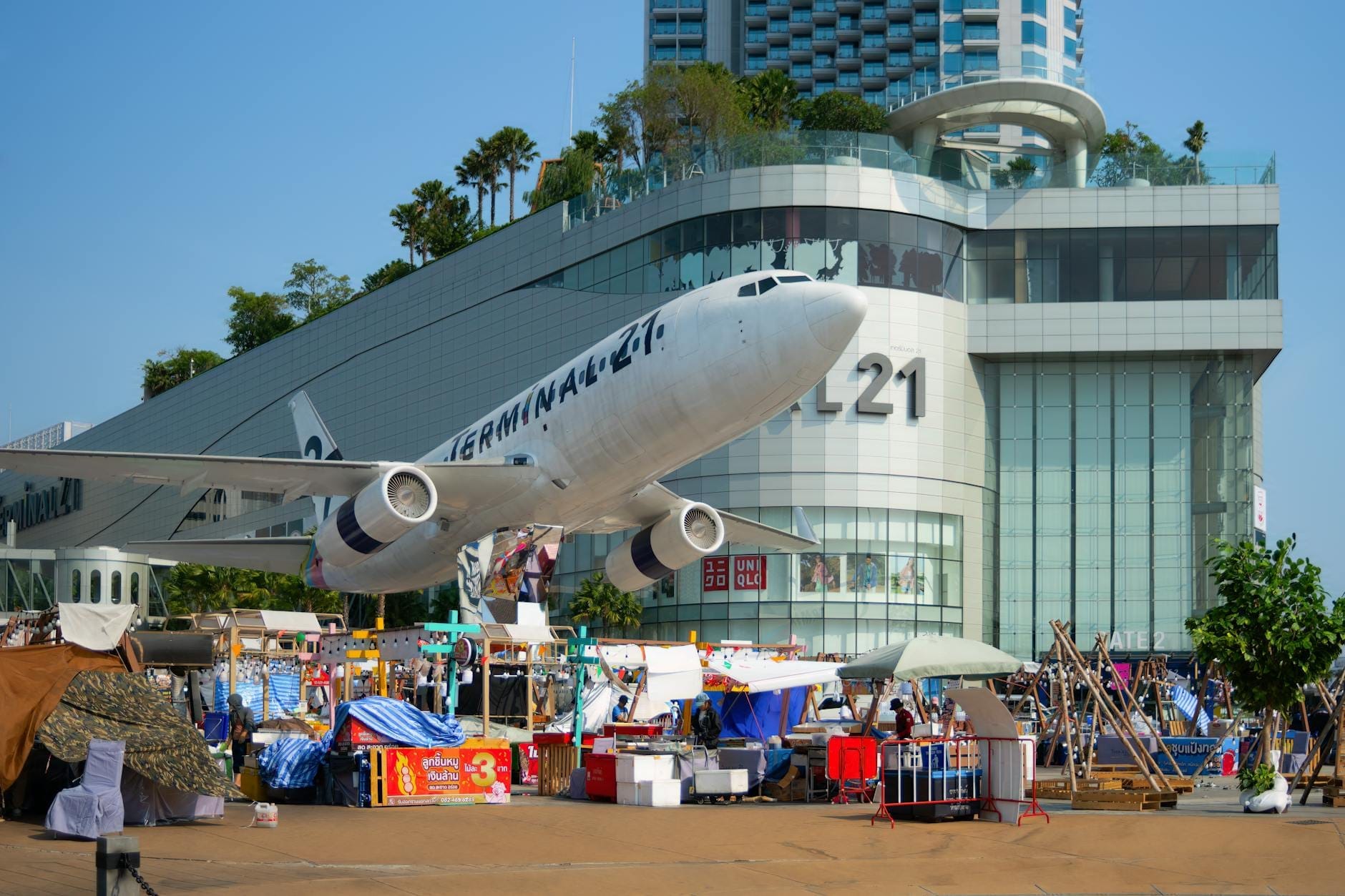 Vista diurna del centro commerciale Terminal 21 Pattaya con la sua iconica installazione di un aereo all'ingresso e i vivaci banchi del mercato all'aperto davanti.