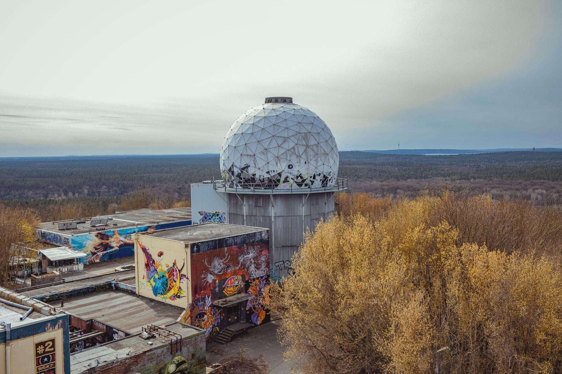La stazione spia di Teufelsberg con la sua iconica cupola radar sopra un edificio ricoperto di graffiti, circondato da alberi e foresta sotto un cielo nuvoloso.