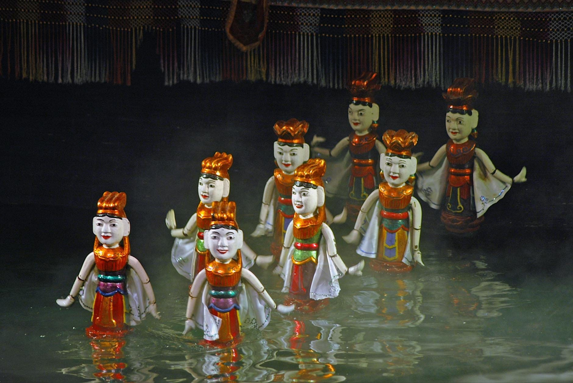 A group of traditional Vietnamese water puppets performing on a misty water stage with dark background at Thang Long Water Puppet Theatre.