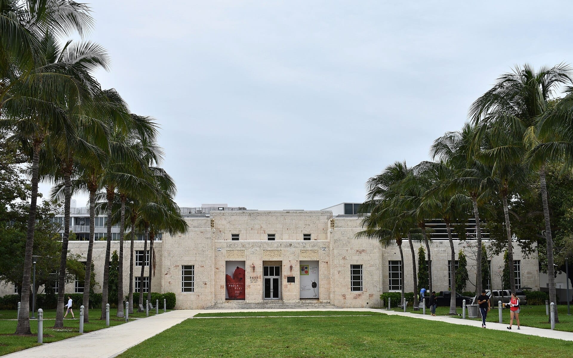 Il Bass Museum a Miami Beach, un edificio beige in stile Art Déco incorniciato da alte palme e un ampio prato in una giornata nuvolosa.