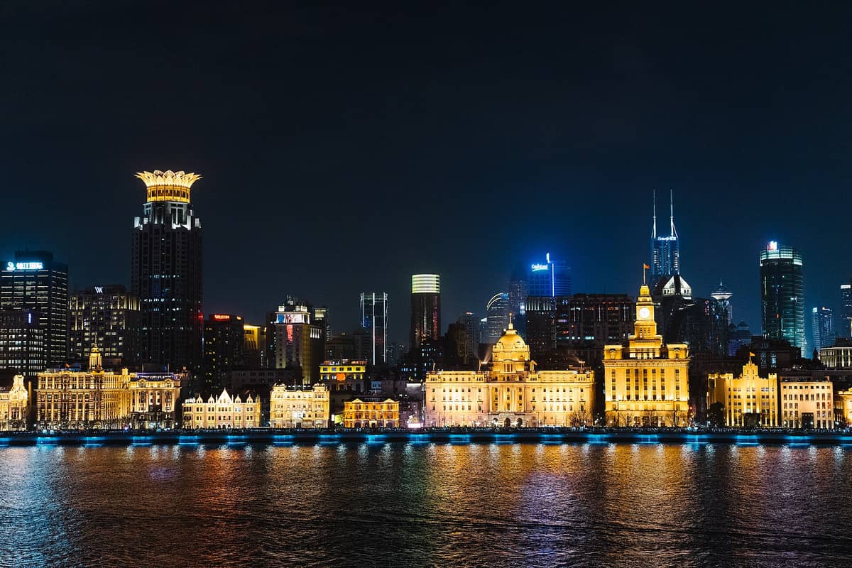 Nächtlicher Blick über den Huangpu auf die ikonische Reihe beleuchteter Gebäude aus dem frühen 20. Jahrhundert am Bund, dahinter die Skyline Shanghais.