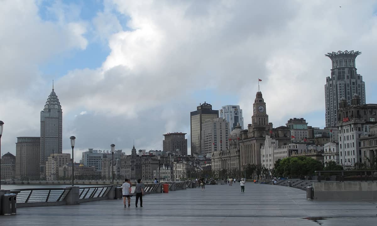 Blick entlang der Bund-Promenade in Shanghai mit Spaziergängern, den ikonischen Kolonialgebäuden und der Shanghaier Skyline an einem bewölkten Tag.