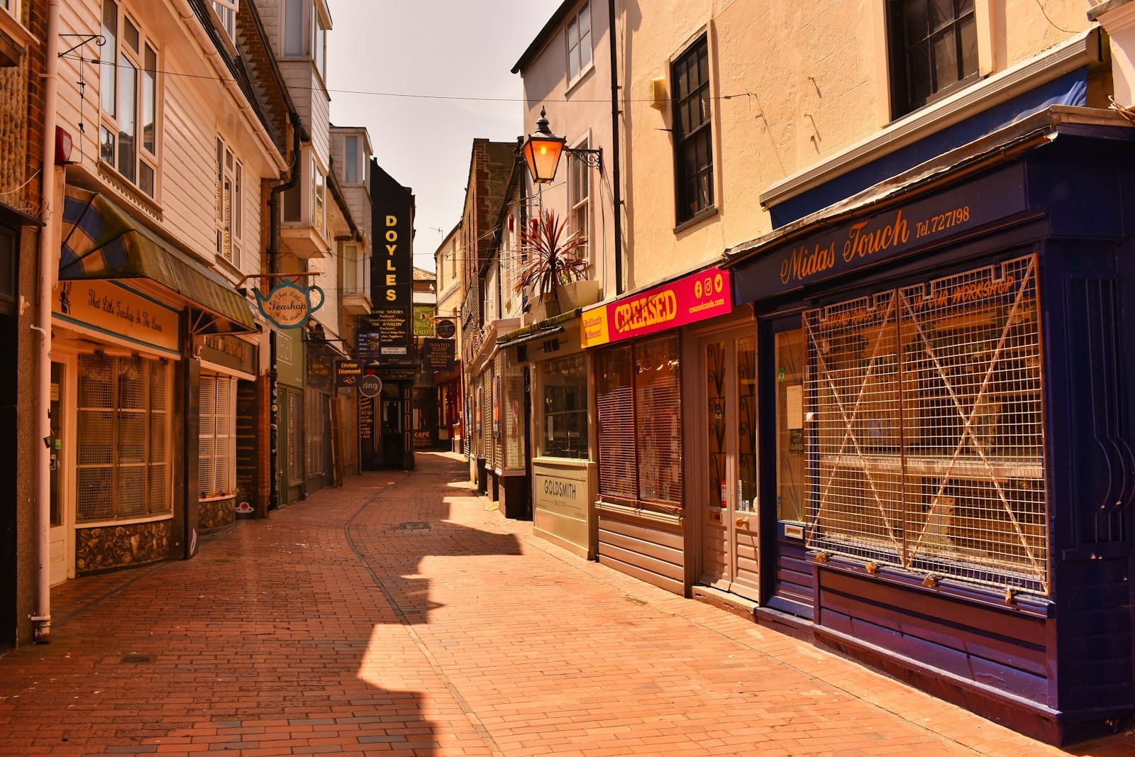 Narrow pedestrian alley in The Lanes, Brighton, lined with historic shops and jewellers, under warm afternoon sunlight with closed storefronts.