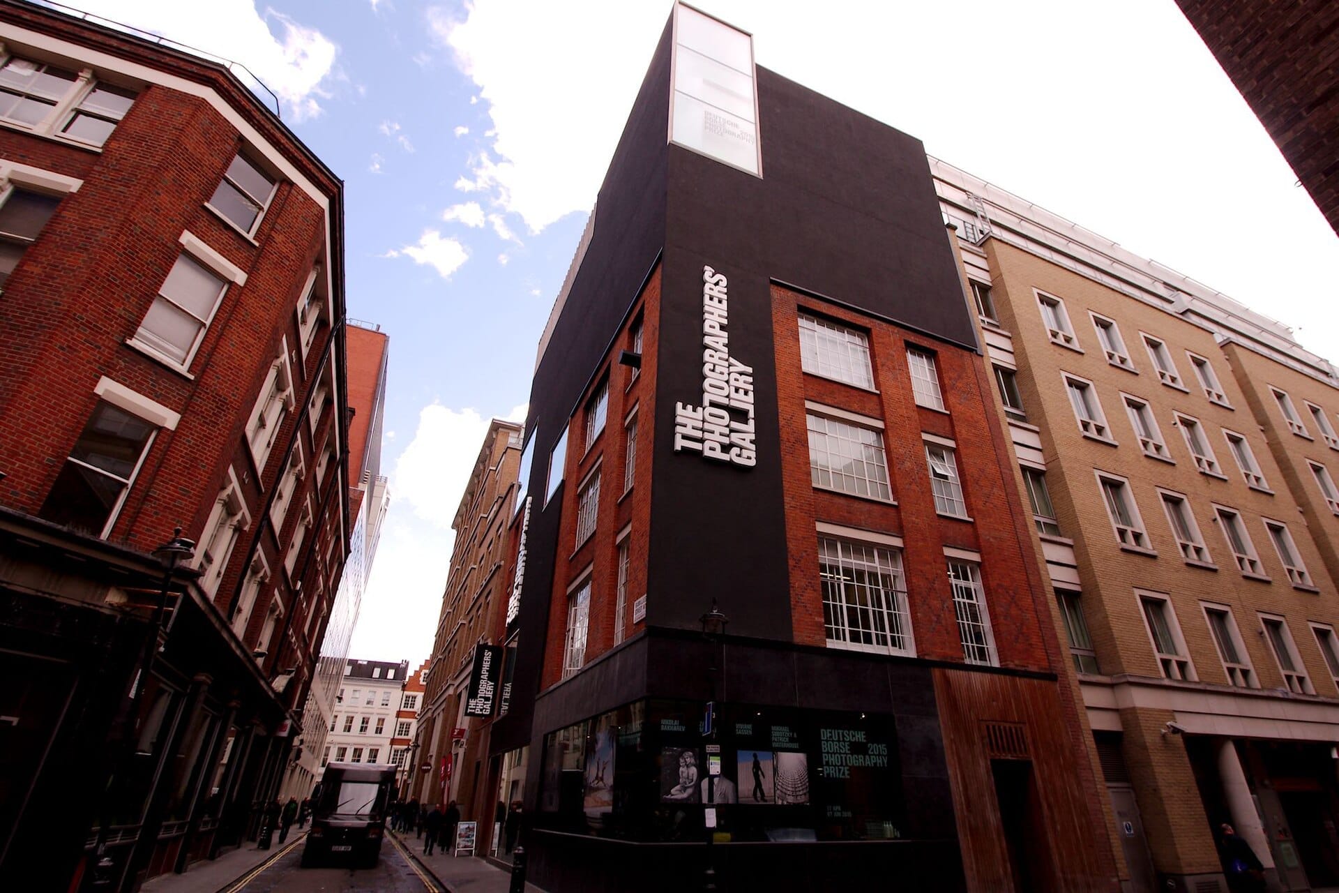 L'edificio della The Photographers' Gallery in Ramillies Street a Londra, con mattoni rossi e rivestimento nero, circondato dall'architettura storica della città.