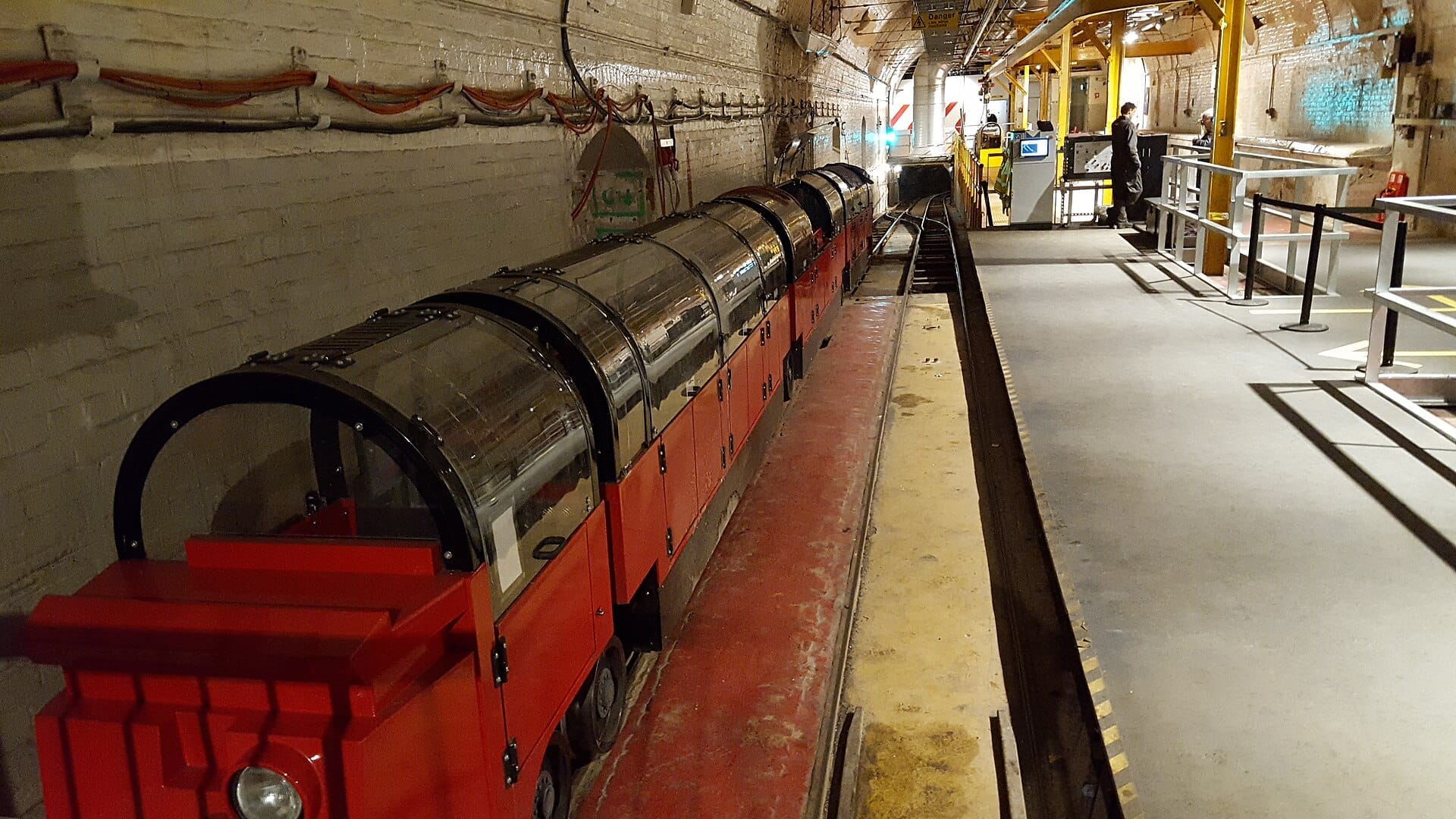 Piccolo treno rosso Mail Rail al The Postal Museum, Londra, parcheggiato all'interno di una stazione sotterranea con visitatori sulla banchina.