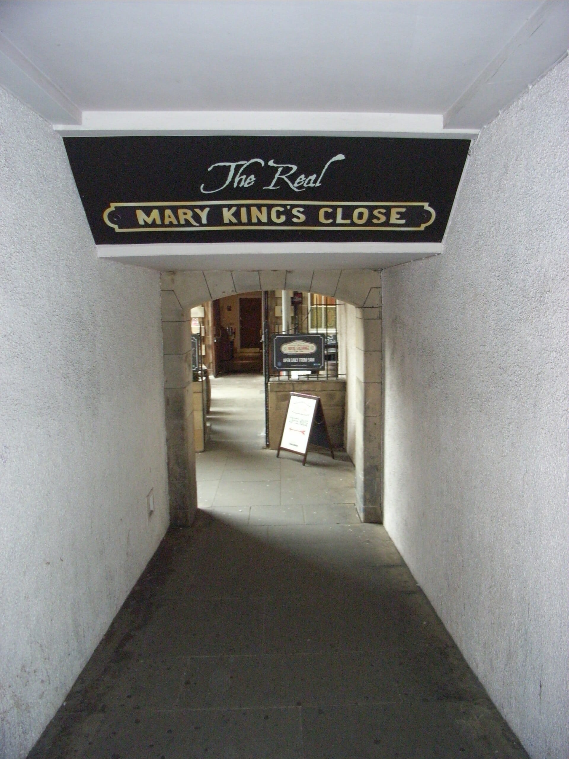 Eingangspassage zu The Real Mary King's Close in Edinburgh, mit einem schwarzen Schild und einem steinernen Torbogen, der zur unterirdischen Attraktion führt.