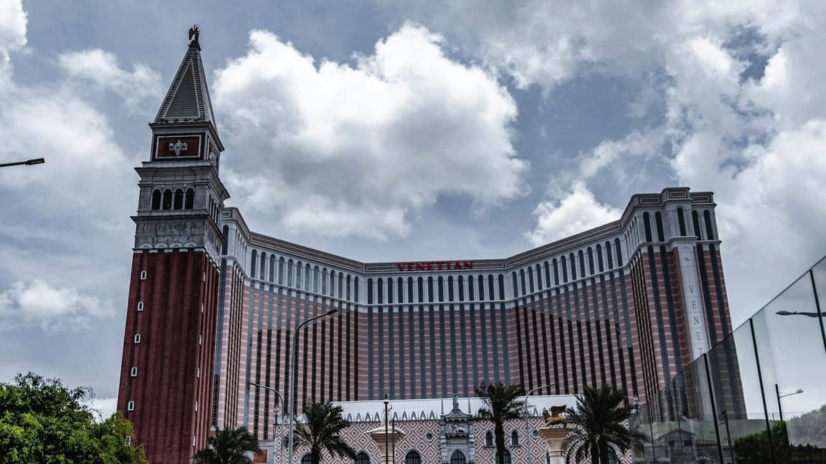 Weitläufige Außenansicht des Venetian Macao unter bewölktem Himmel, mit der markanten rot-weißen Fassade und dem unverkennbaren Uhrenturm.