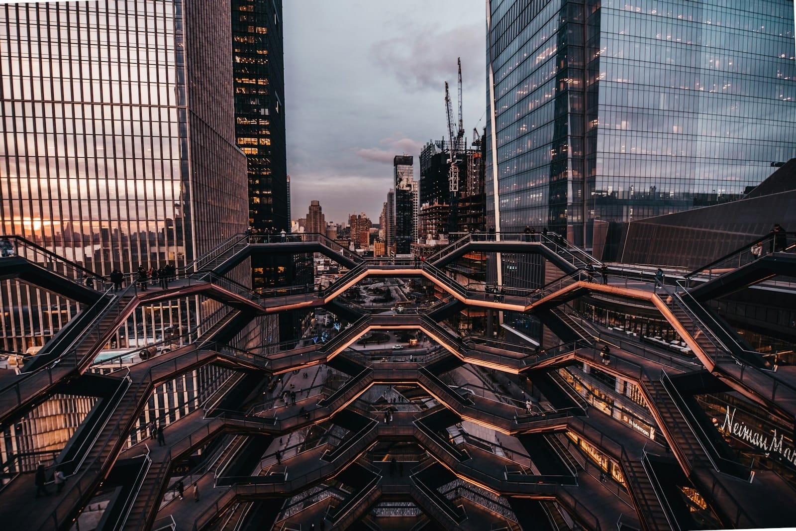 Le scale geometriche color rame del Vessel incorniciate dai grattacieli di Hudson Yards al tramonto, con una vista suggestiva della struttura e del panorama cittadino circostante.
