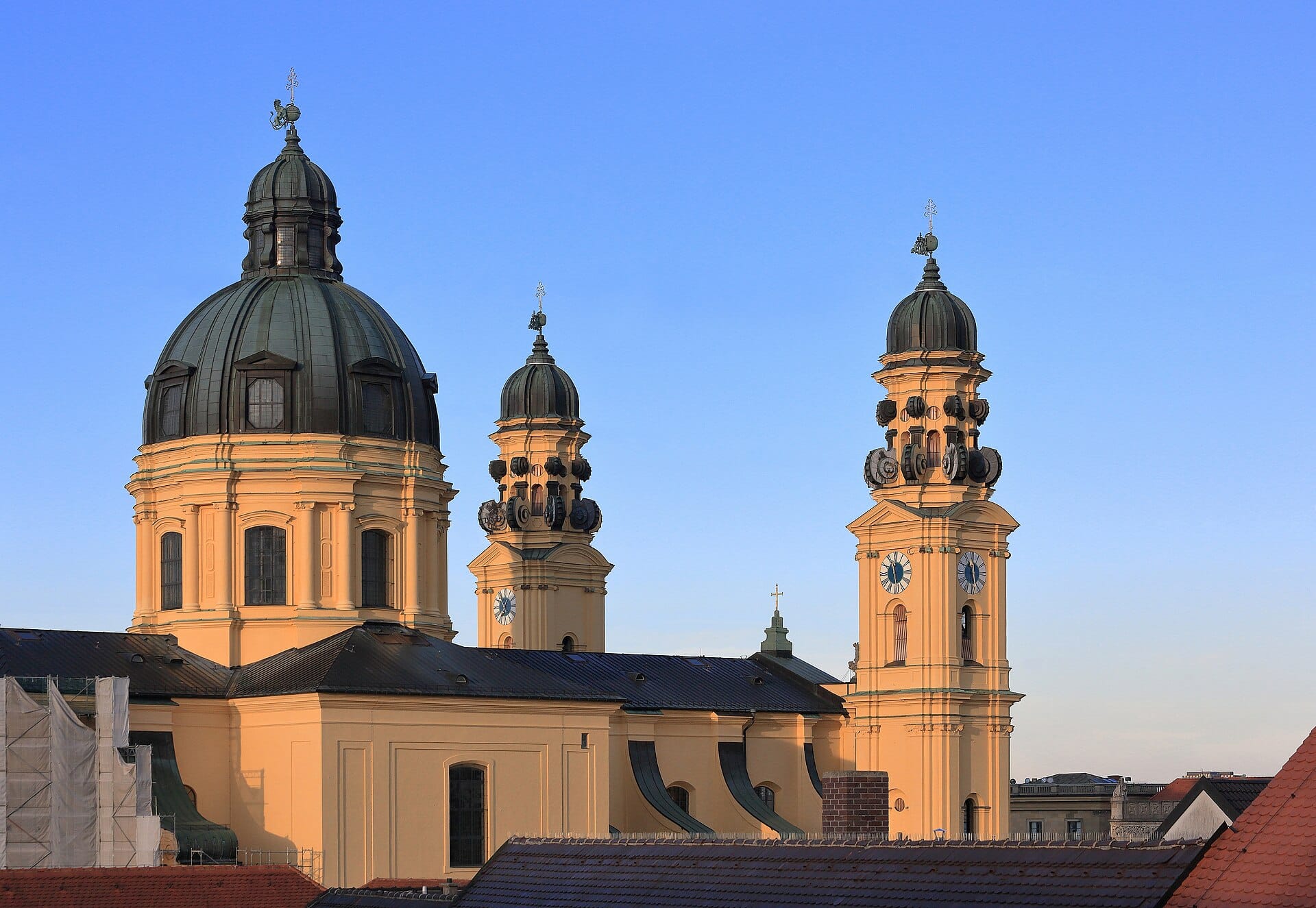 โดมสีเหลืองอมน้ำตาลและหอระฆังคู่ของ Theatinerkirche St. Kajetan โดดเด่นใต้ท้องฟ้าสีฟ้าใส เป็นซิลูเอตต์แลนด์มาร์กแห่งมิวนิกที่ใครก็จำได้