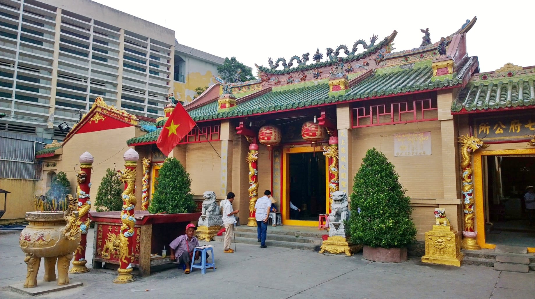 La entrada de la Pagoda Thiên Hậu en Cholon, con elaboradas columnas de dragones, estatuas de leones y visitantes bajo un cielo nublado.