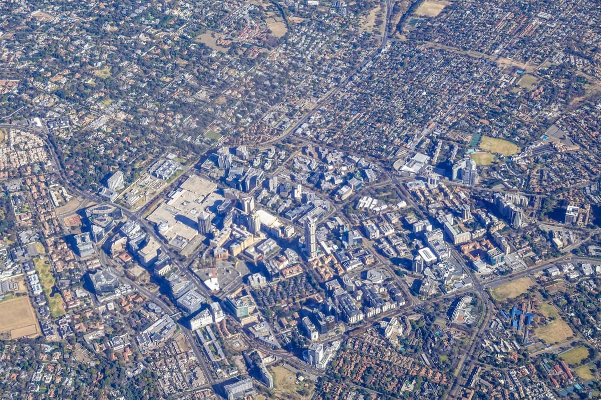 Aerial view of Adelaide city centre showing the grid layout and surrounding green parklands, with suburbs spreading out around the CBD.