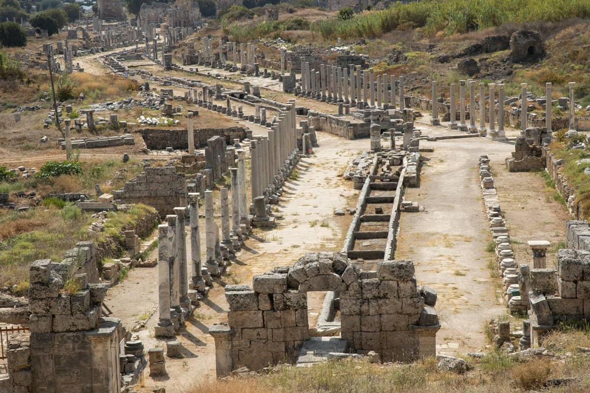 A sweeping view of ancient city ruins with long rows of stone columns and scattered masonry, under a clear sky near Antalya.