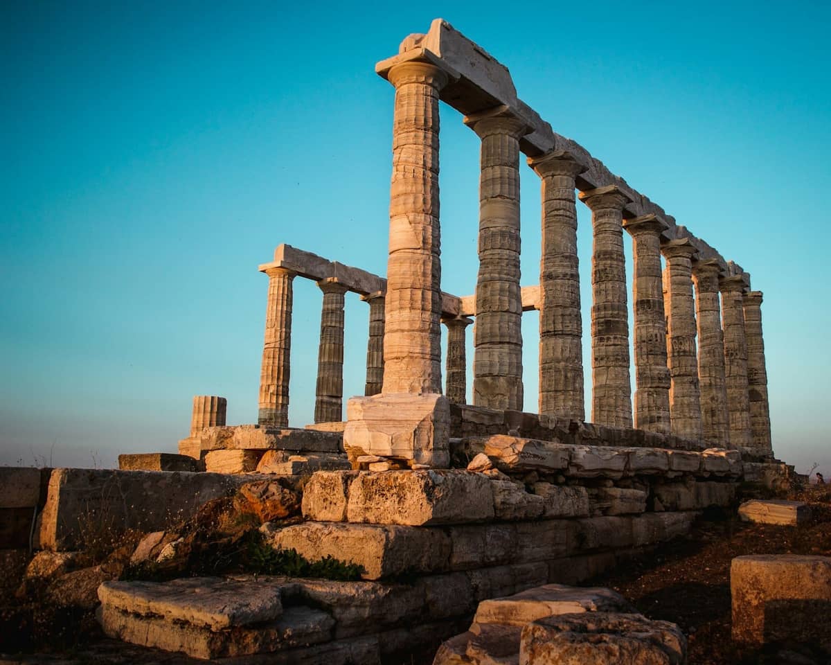 Vista iluminada por el sol del Templo de Poseidón en Cabo Sounion con cielo azul despejado y antiguas columnas de piedra.