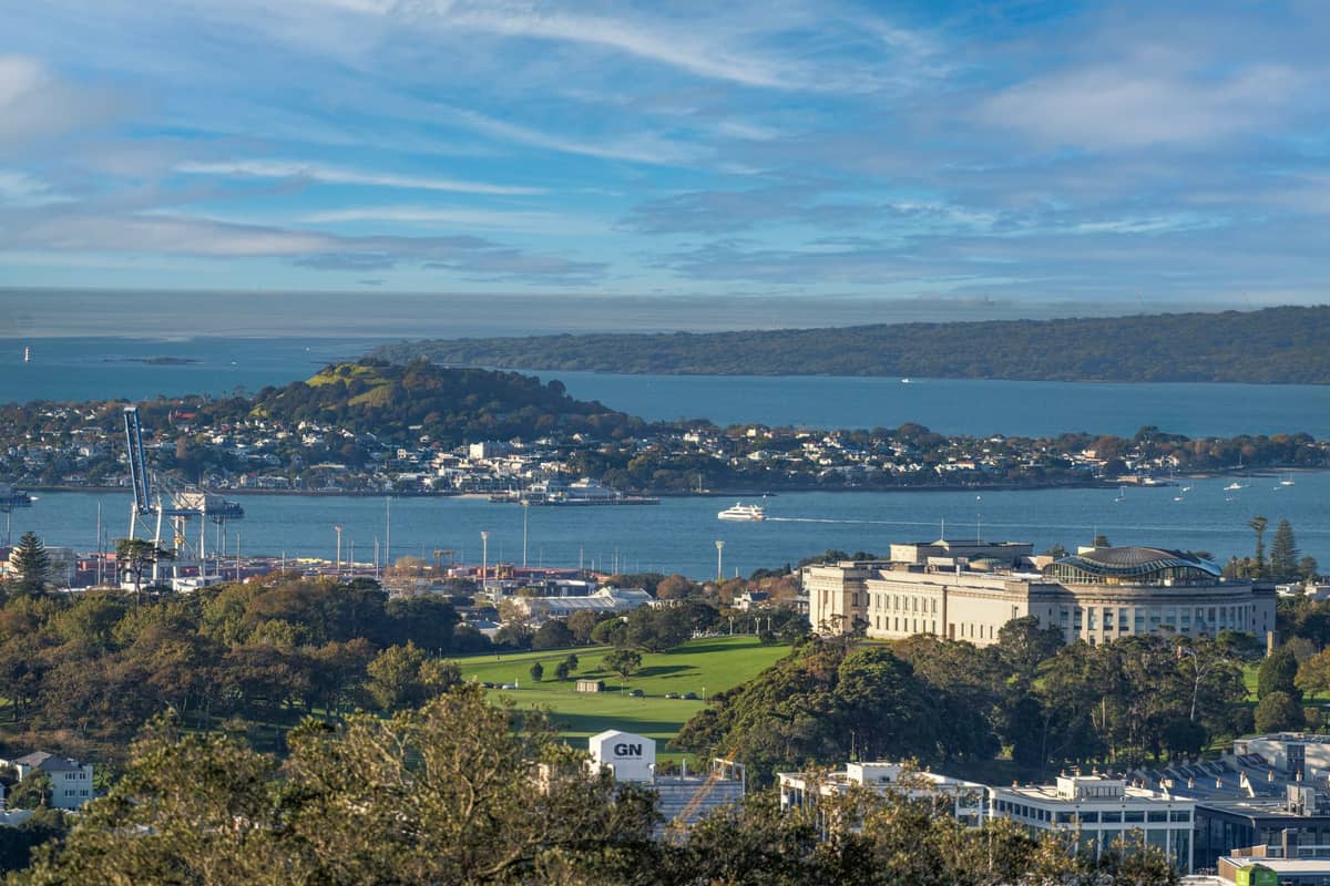 Vista del Museo de Auckland con un prominente cono volcánico y la isla Rangitoto al fondo, al otro lado del puerto bajo un cielo azul.