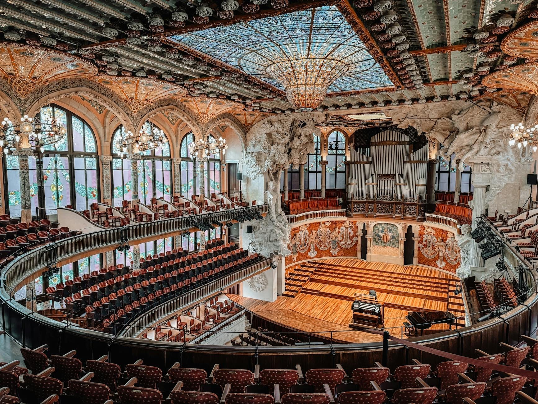 Wide-angle view of Palau de la Música Catalana’s ornate concert hall with stained glass ceiling, organ pipes, and elegant balconies in Barcelona.