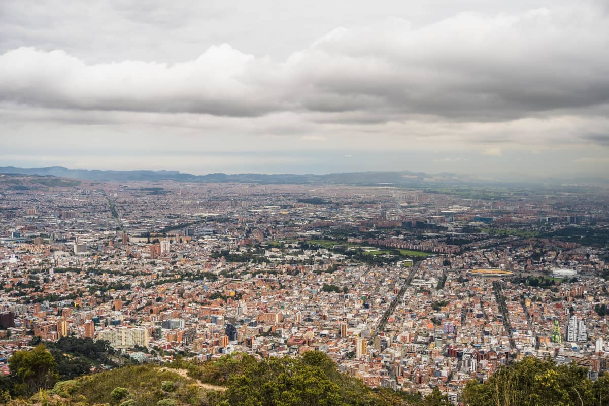 Sweeping panoramic view of Bogotá city stretching to the horizon, taken from a high vantage point with cloudy skies above.