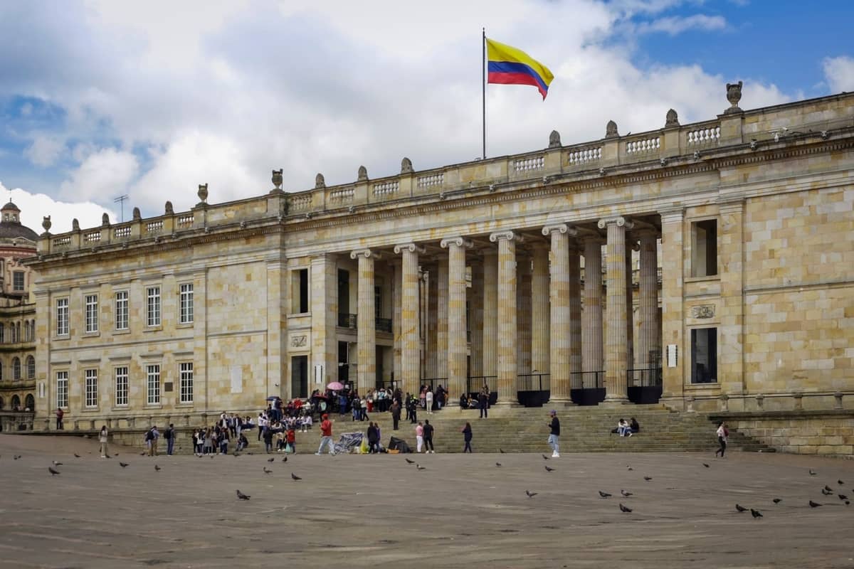 Wide view of Colombia’s Capitol building in Bogotá’s historic center, with people and pigeons in the large square in front.