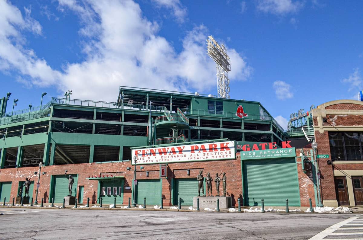 Vista esterna di Fenway Park con le sue pareti verdi, l'insegna rossa, i cancelli d'ingresso e le statue sotto un cielo azzurro