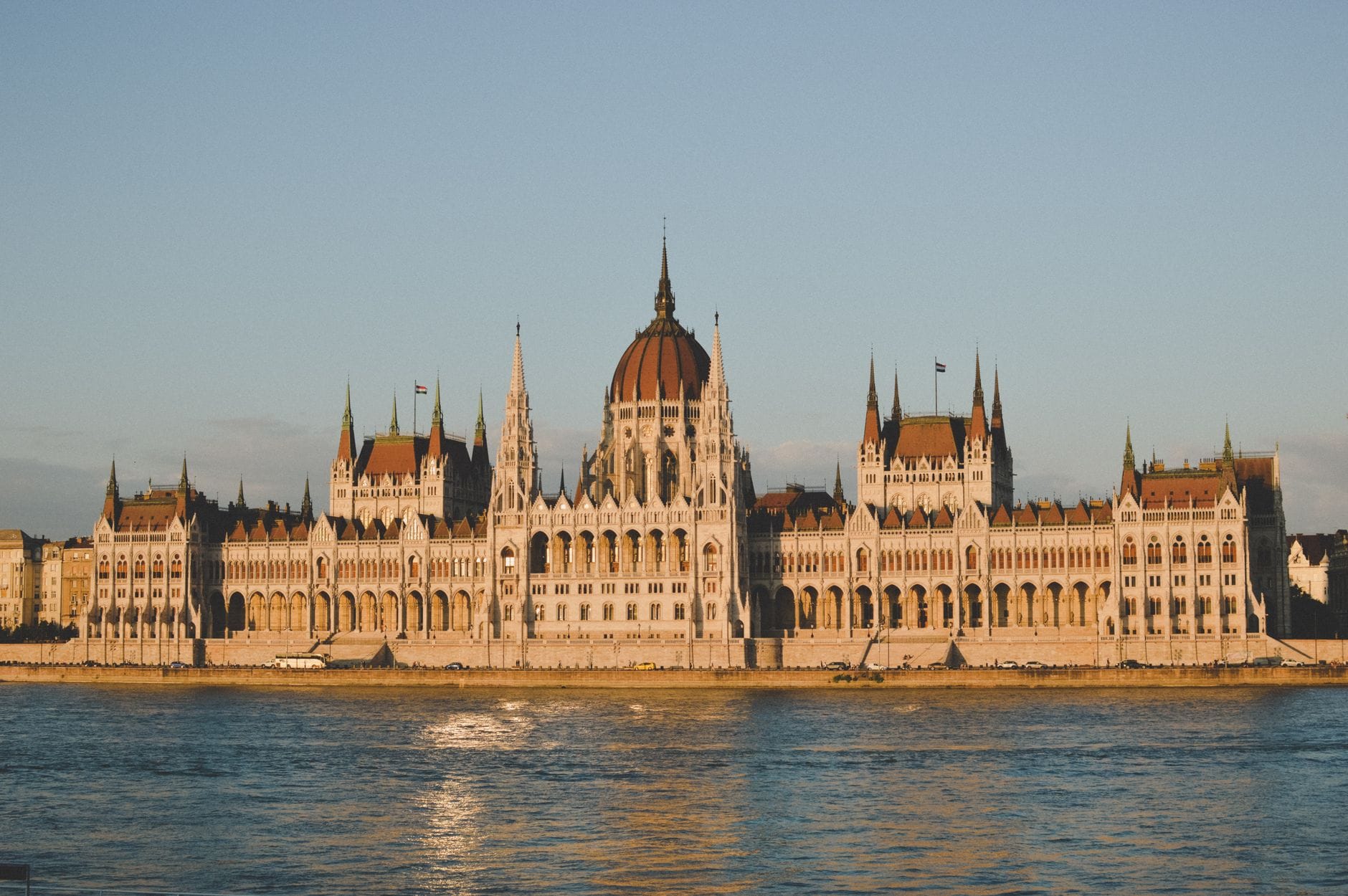 Das Parlamentsgebäude von Budapest im Sonnenlicht vom anderen Ufer der Donau aus gesehen, mit seiner ikonischen Kuppel und den deutlich sichtbaren Türmen.