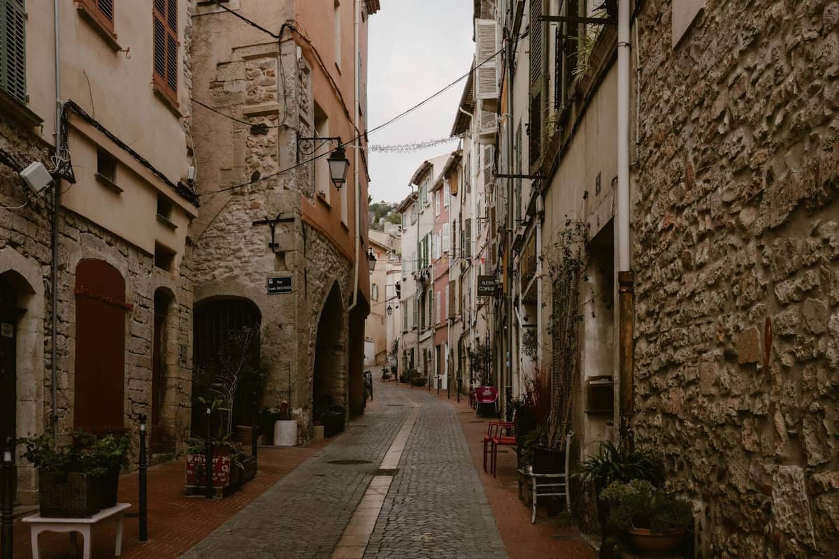 Calle estrecha empedrada flanqueada de antiguos edificios de piedra y ventanas con postigos en el barrio antiguo de Le Suquet en Cannes.