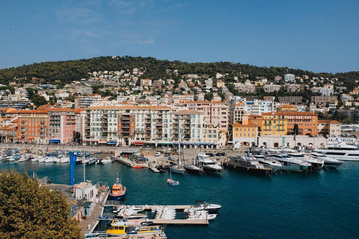 Vista panorámica de un puerto con yates y coloridos edificios al fondo, frente a una ladera en Cannes en un día soleado.