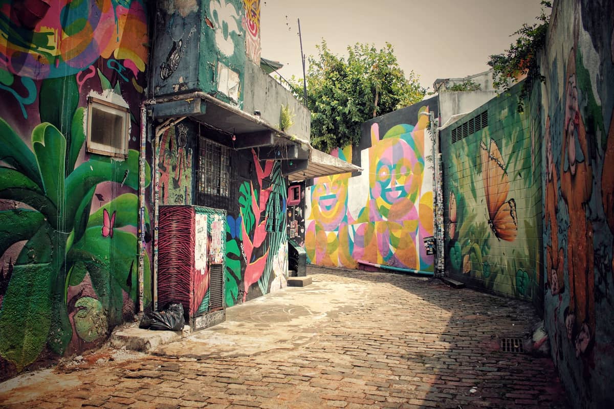Narrow alley in Cartagena with colorful street art murals covering the walls, showing vibrant faces, plants, and butterflies.