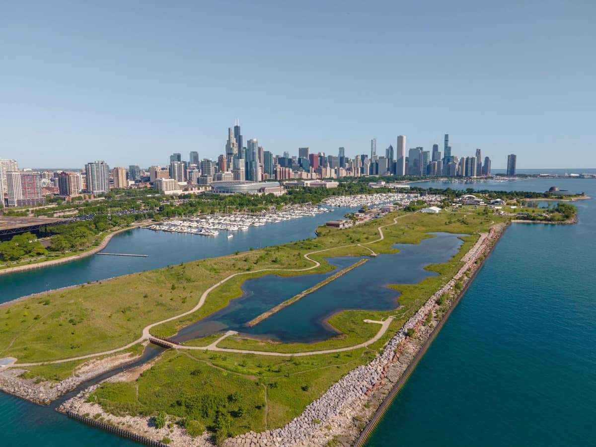 Luftaufnahme der Skyline von Chicago und des Lake Michigan mit einem Yachthafen und einem Park im Vordergrund an einem strahlend sonnigen Tag.