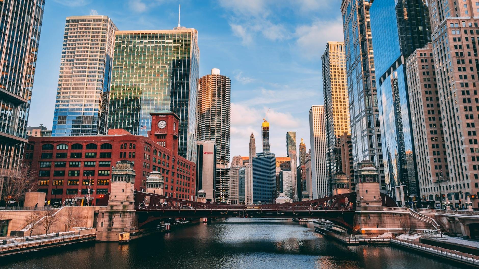 Vista deslumbrante do skyline do centro de Chicago ao pôr do sol, com arranha-céus refletidos no rio e uma ponte histórica em primeiro plano.