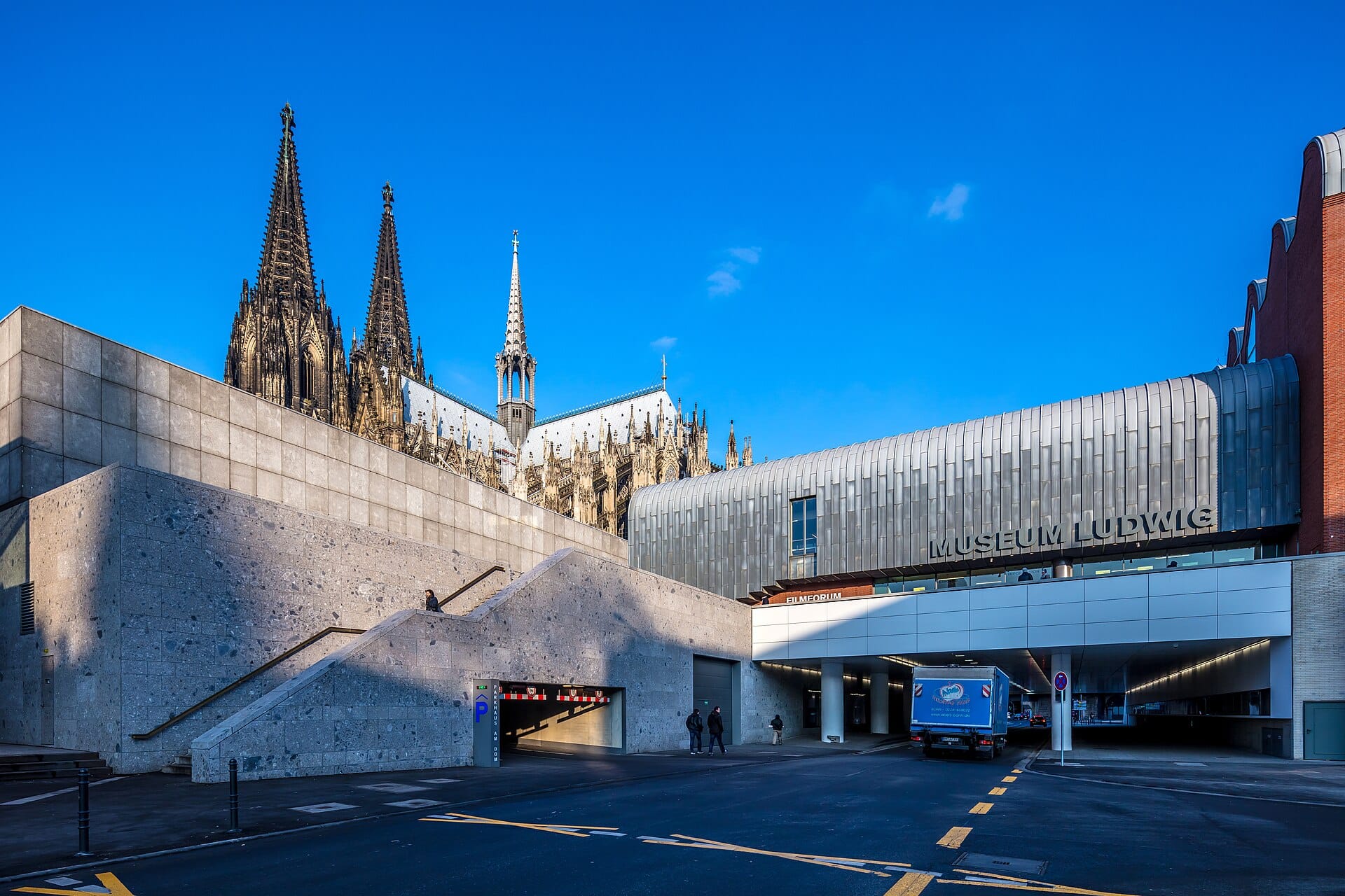 ภายนอกของ Museum Ludwig ในเมือง Cologne พร้อมสถาปัตยกรรมสมัยใหม่อันโดดเด่น และยอดแหลมของ Cologne Cathedral ที่ตระหง่านอยู่เบื้องหลัง