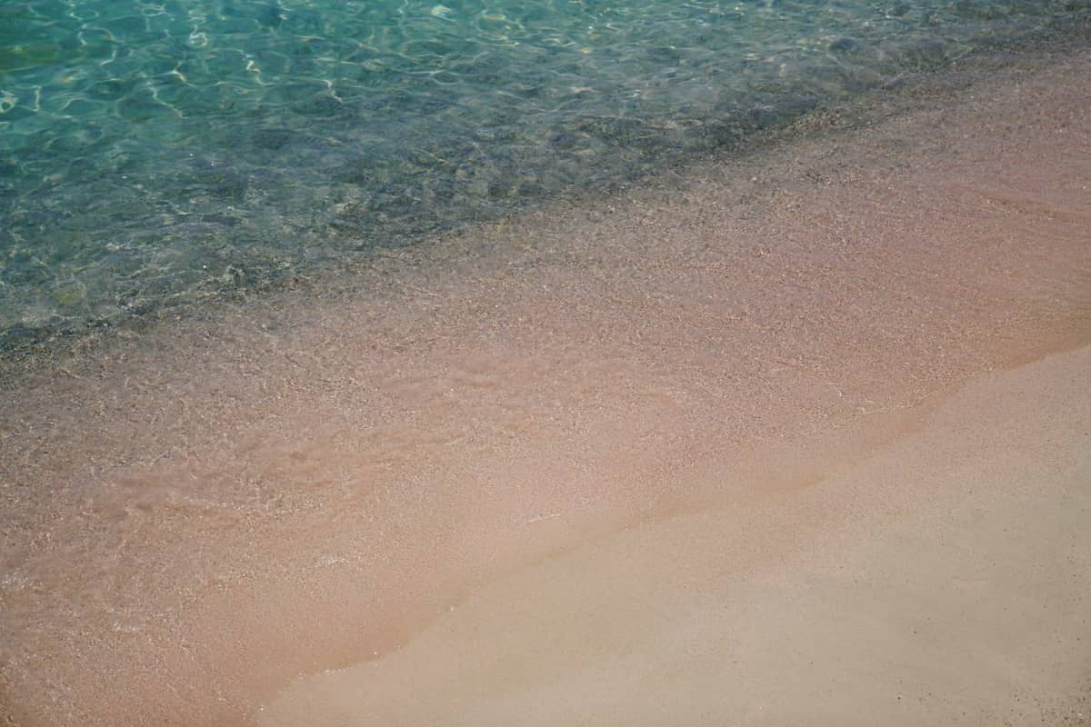 Belirgin pembe tonuyla kumlu bir plajla buluşan berrak, turkuaz su — Girit'teki Elafonissi Beach'in klasik bir görünümü.