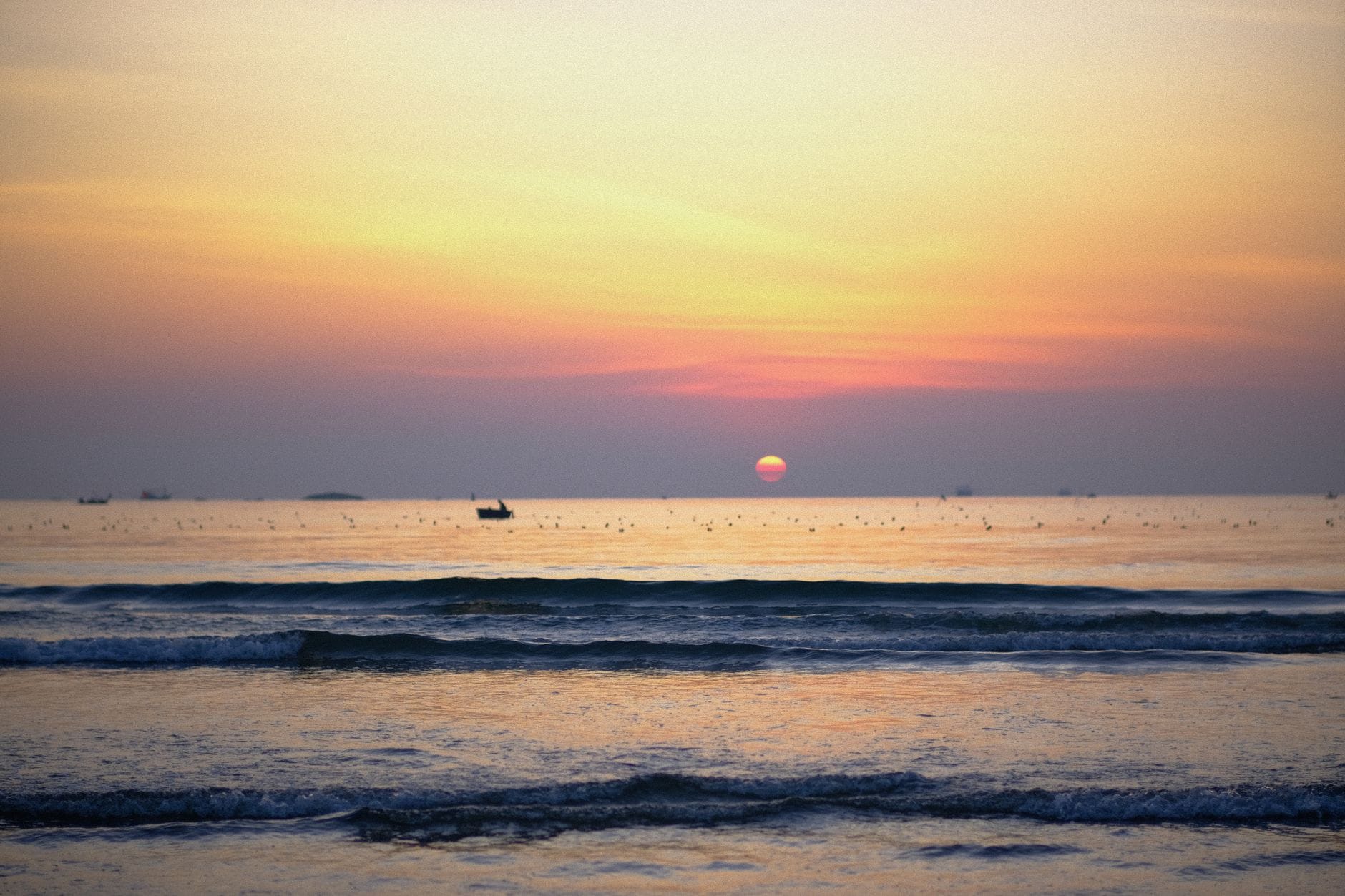 ทัศนียภาพชายหาดอันเงียบสงบที่ Da Nang ยามพระอาทิตย์ขึ้น พร้อมคลื่นเบาๆ เรือบนผืนน้ำ และท้องฟ้าสีสันสดใส