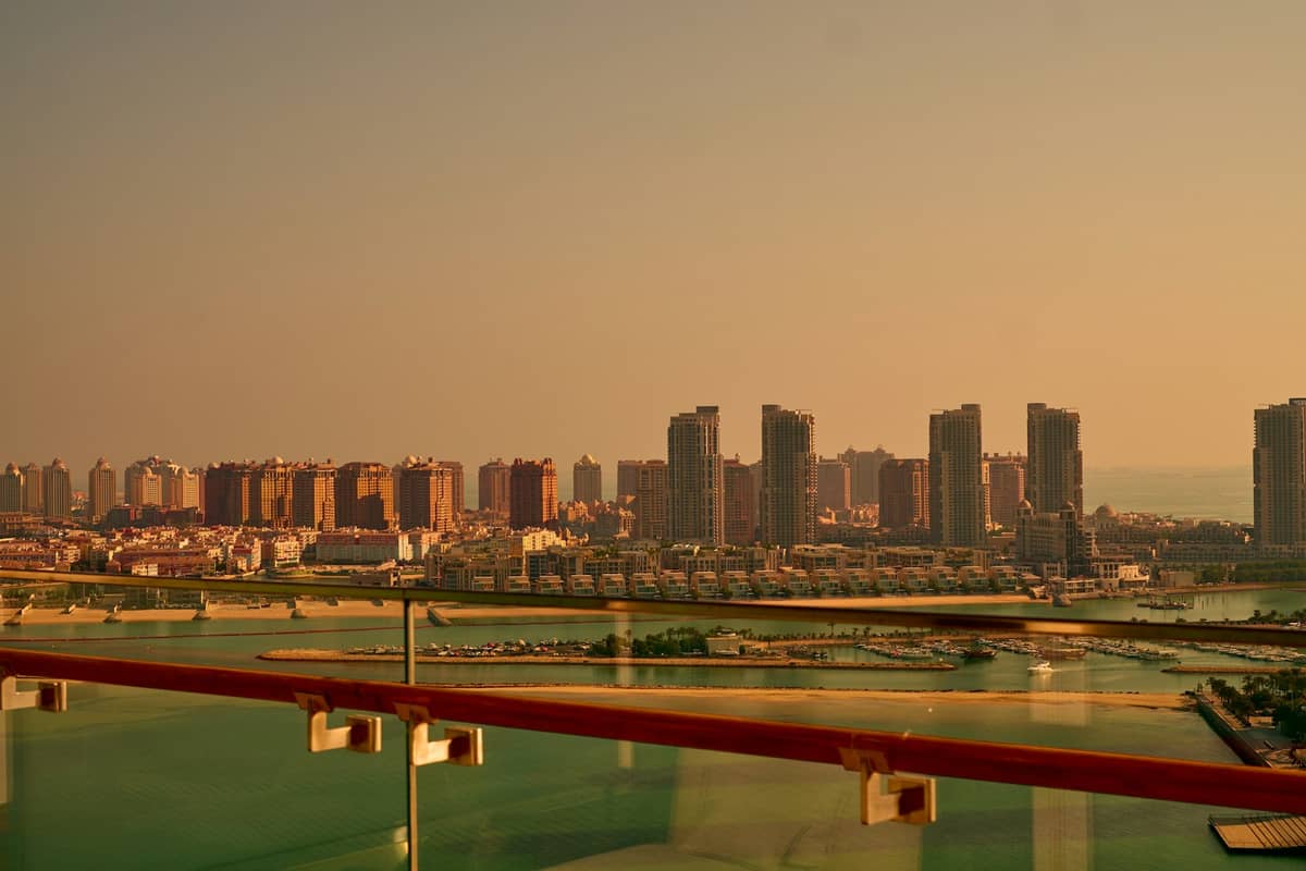 Luftaufnahme von The Pearl in Doha mit seinen Wohntürmen, dem Yachthafen und türkisfarbenen Wasserwegen bei Sonnenuntergang.