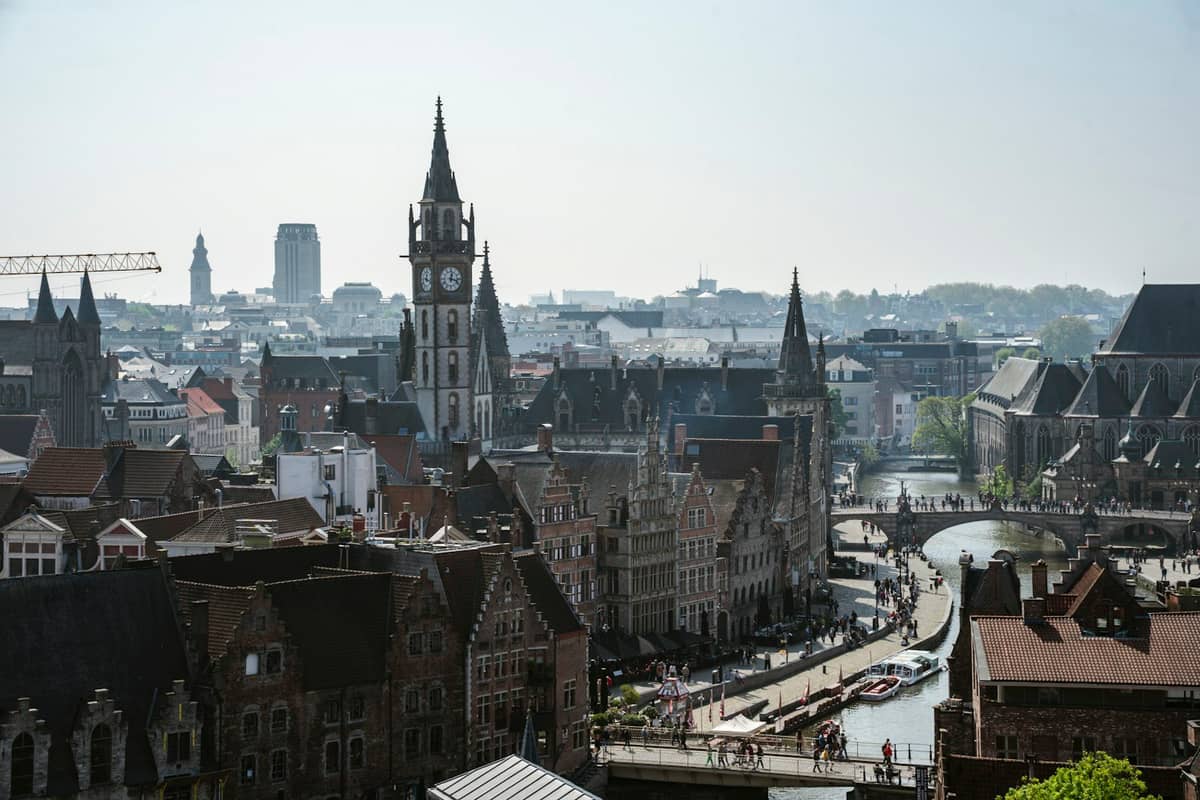 Aerial view of Ghent’s old town with medieval towers, rivers, canals, and bustling waterfront streets on a sunny day