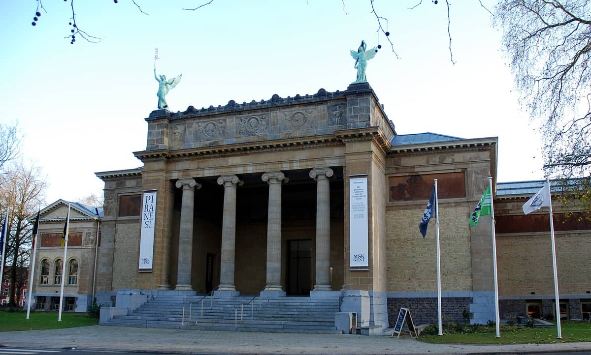 Front view of Ghent’s Museum of Fine Arts (MSK Gent) with its grand columns, statues, and flags, seen under a clear sky.