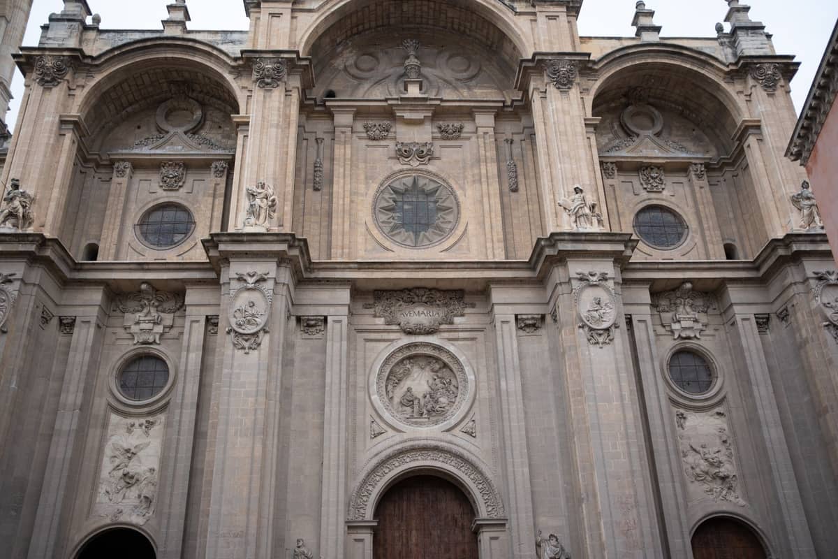 มุมมองระยะใกล้ของด้านหน้าอาคารสไตล์เรเนซองส์อันวิจิตรของมหาวิหาร Granada พร้อมประตูโค้ง รายละเอียดหินแกะสลัก และหน้าต่างทรงกลม
