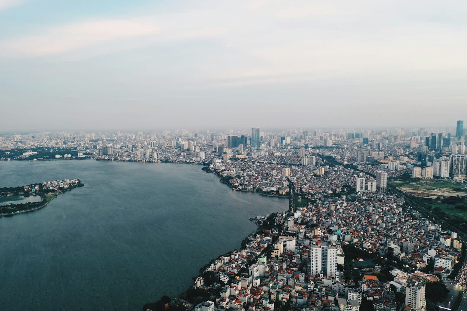 Aerial view of Hanoi's West Lake and surrounding city skyline with dense urban buildings and high-rise towers.