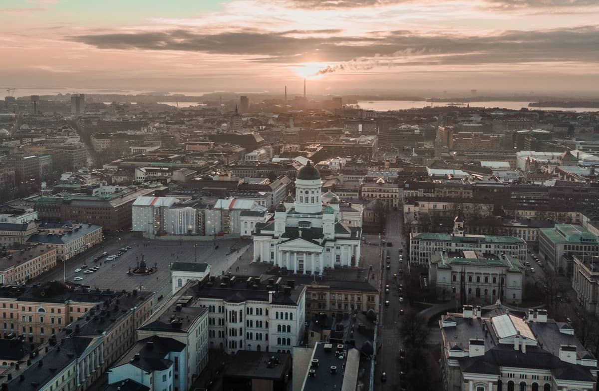 Vista aérea de Helsinque ao pôr do sol, com a Catedral de Helsinque em destaque no centro e a paisagem urbana se estendendo em direção à orla marítima.