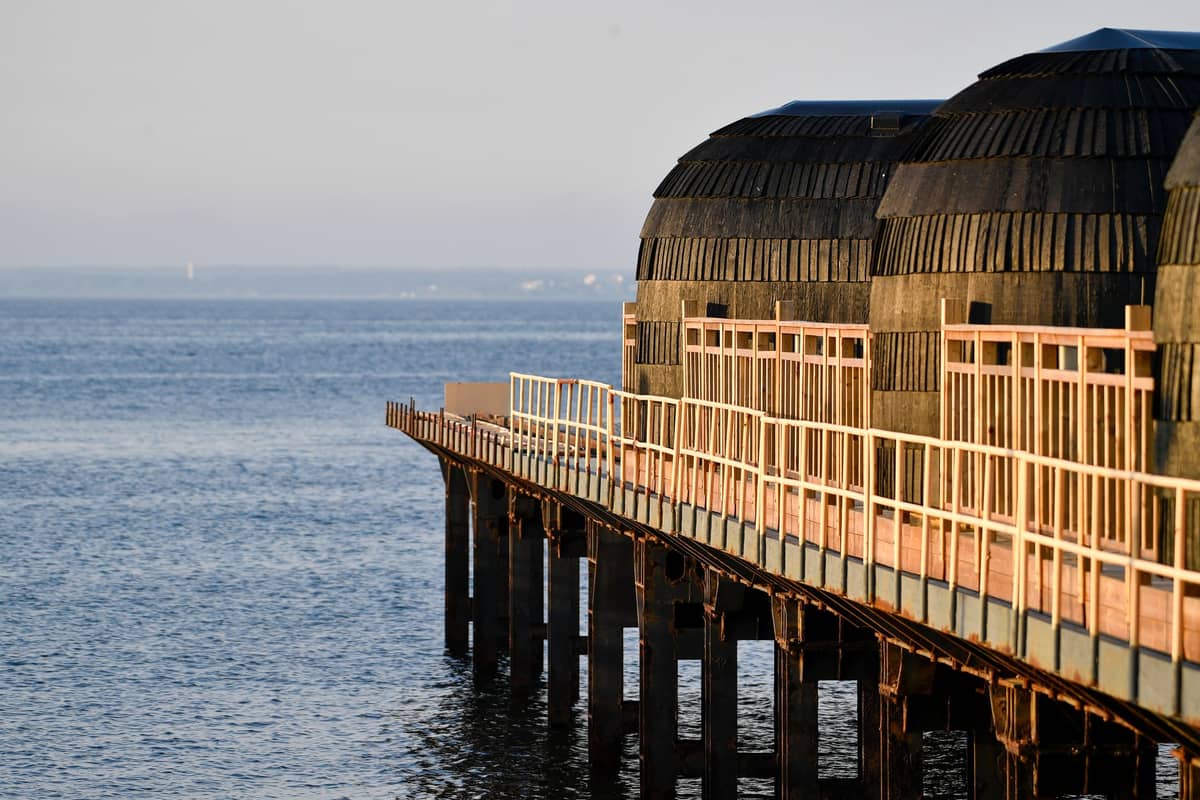 Impressionantes estruturas de sauna redondas de madeira em um píer sobre o mar com uma suave luz dourada, representando as únicas experiências de sauna em Helsinki.