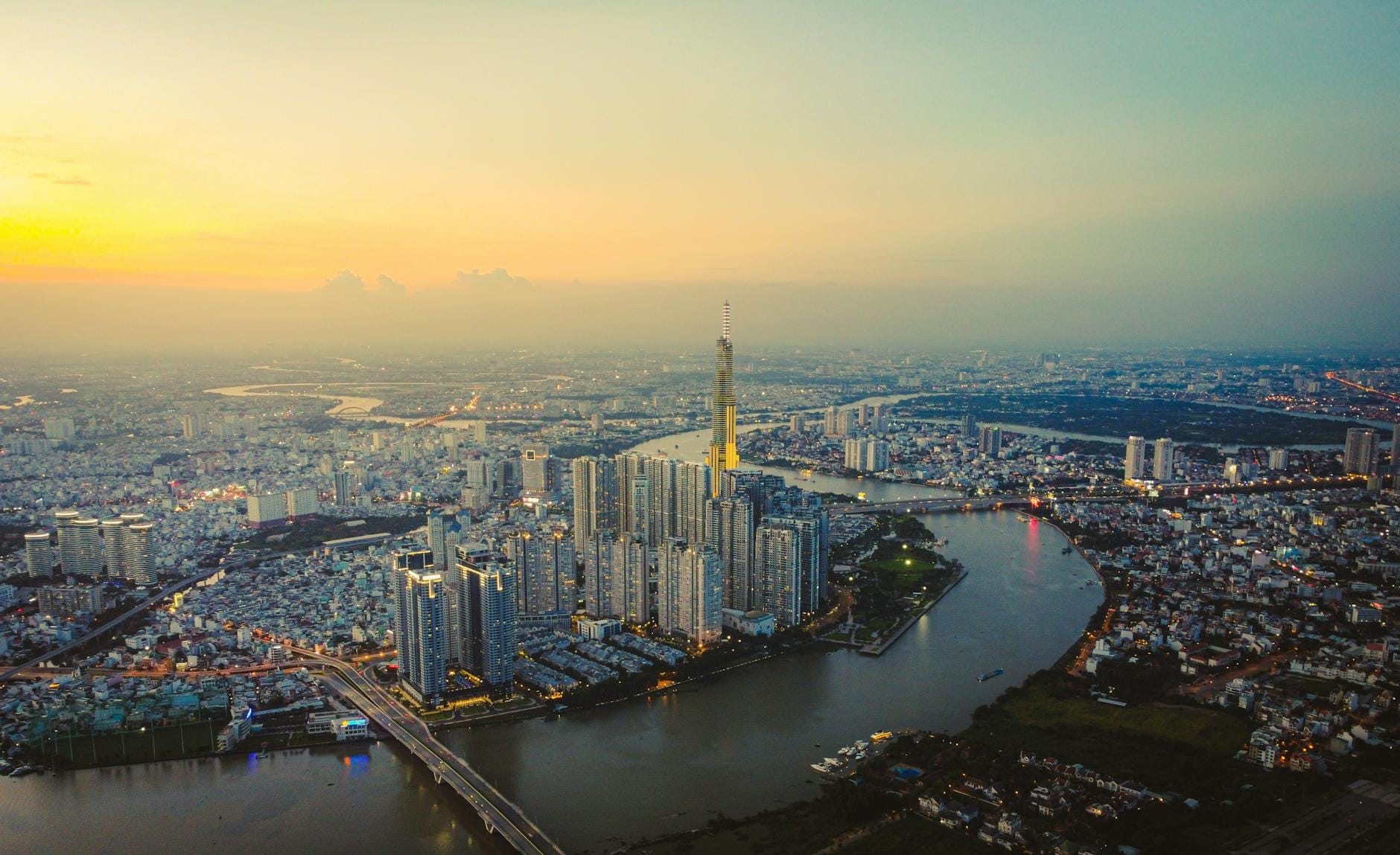 Vista aérea del horizonte de Ho Chi Minh City con la torre Landmark 81, un meandro del río y edificios al atardecer bajo un cielo colorido.