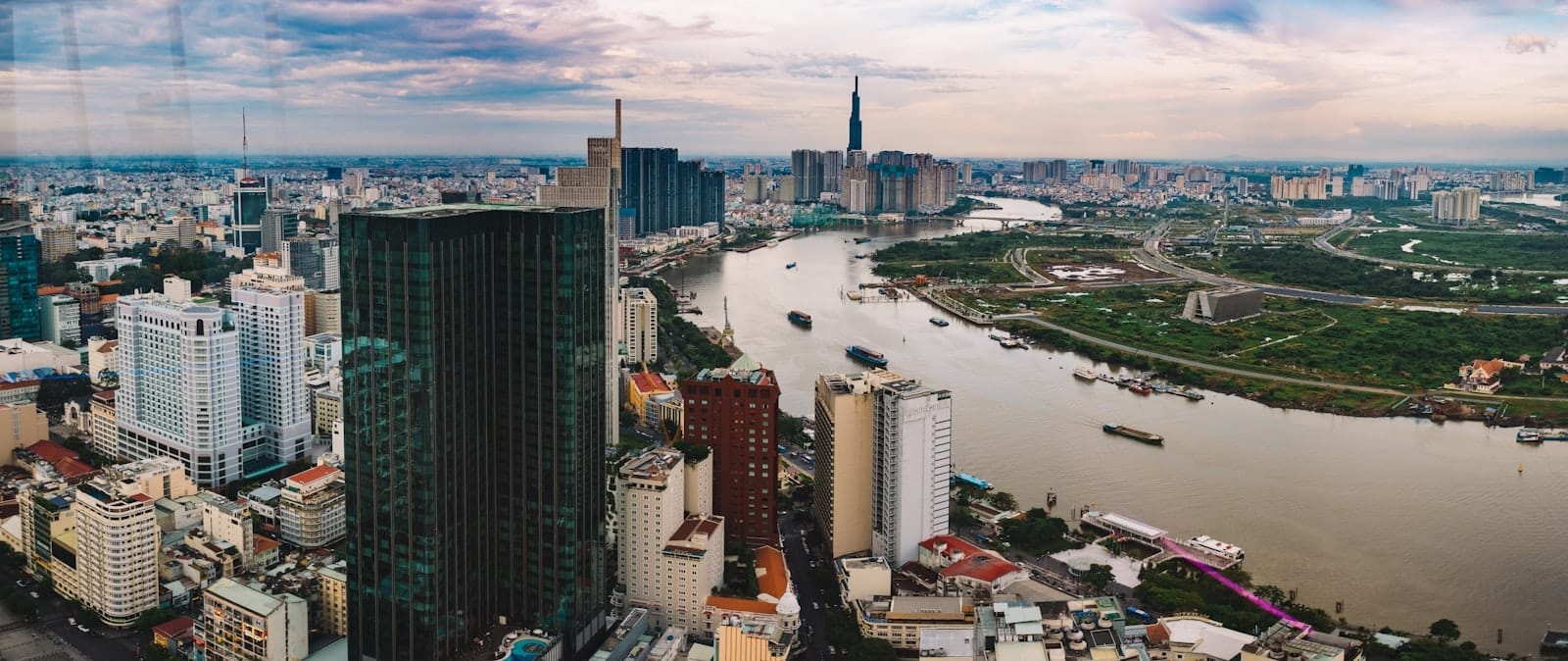 Vista aérea panorámica del horizonte de Ciudad Ho Chi Minh a lo largo del río Saigón, con rascacielos, una densa trama urbana y un dramático cielo al atardecer.
