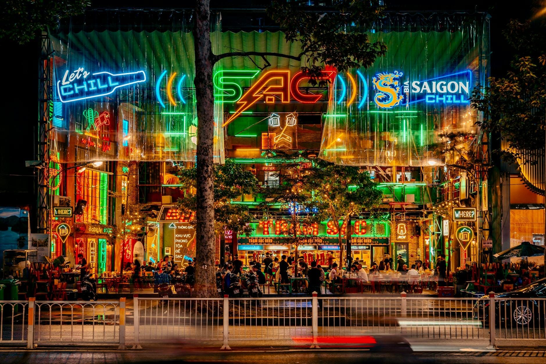 Una calle vibrante y concurrida en Ho Chi Minh City iluminada por coloridos letreros de neón y llena de personas disfrutando del animado ambiente nocturno.