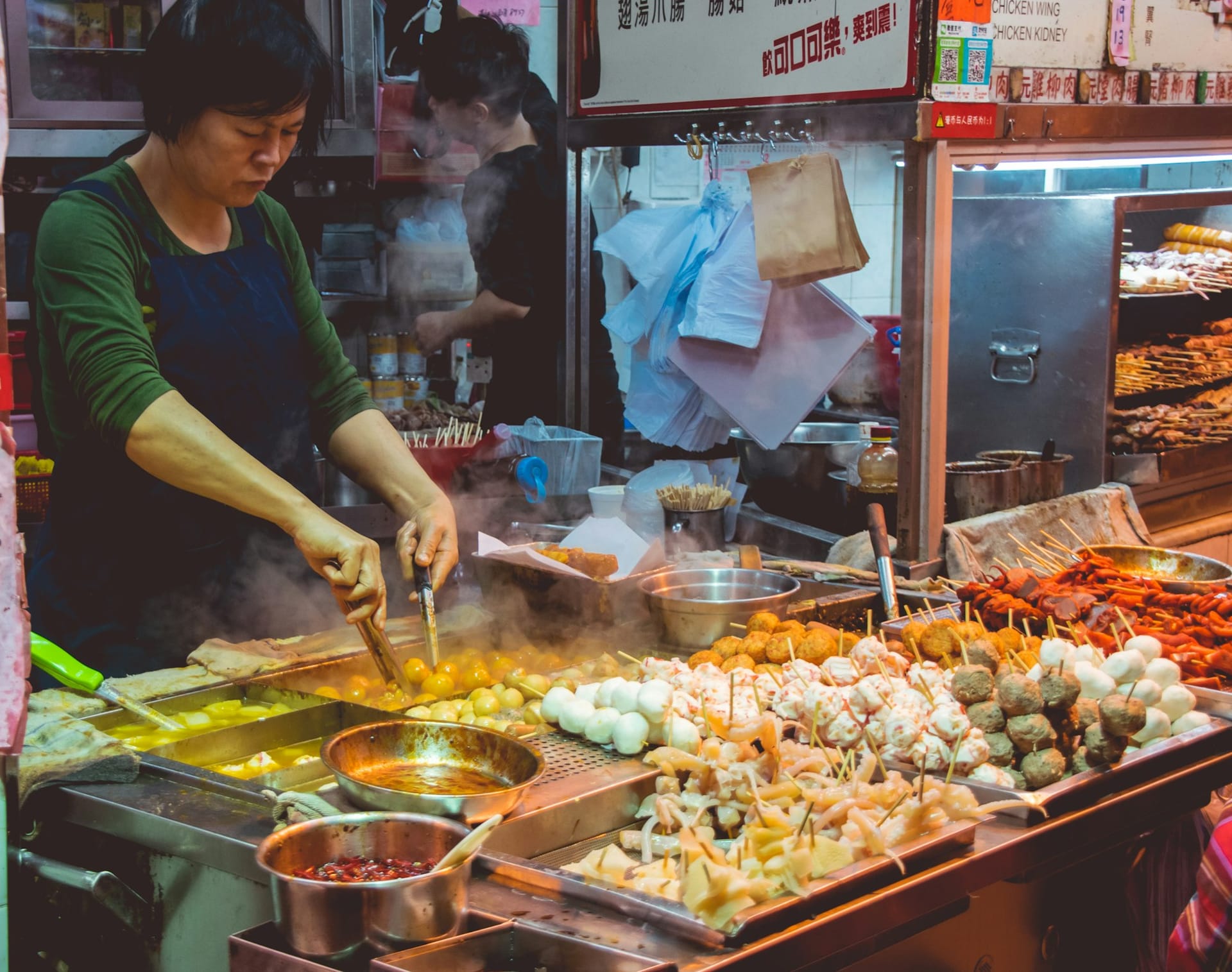 Étal de street food à Hong Kong au marché de nuit avec boulettes de poisson, brochettes et woks.